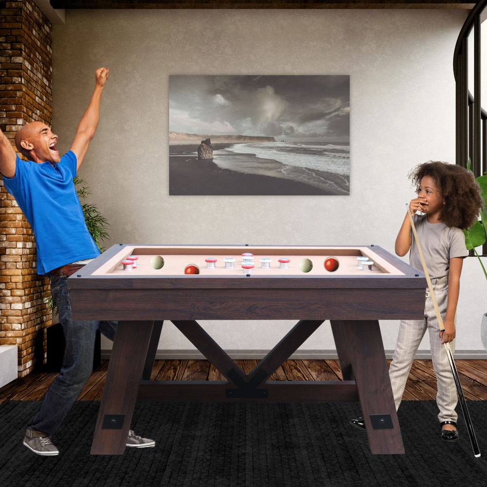 Two people playing pool in a room with a beach-themed painting on the wall.