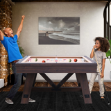 Two people playing pool in a room with a beach-themed painting on the wall.