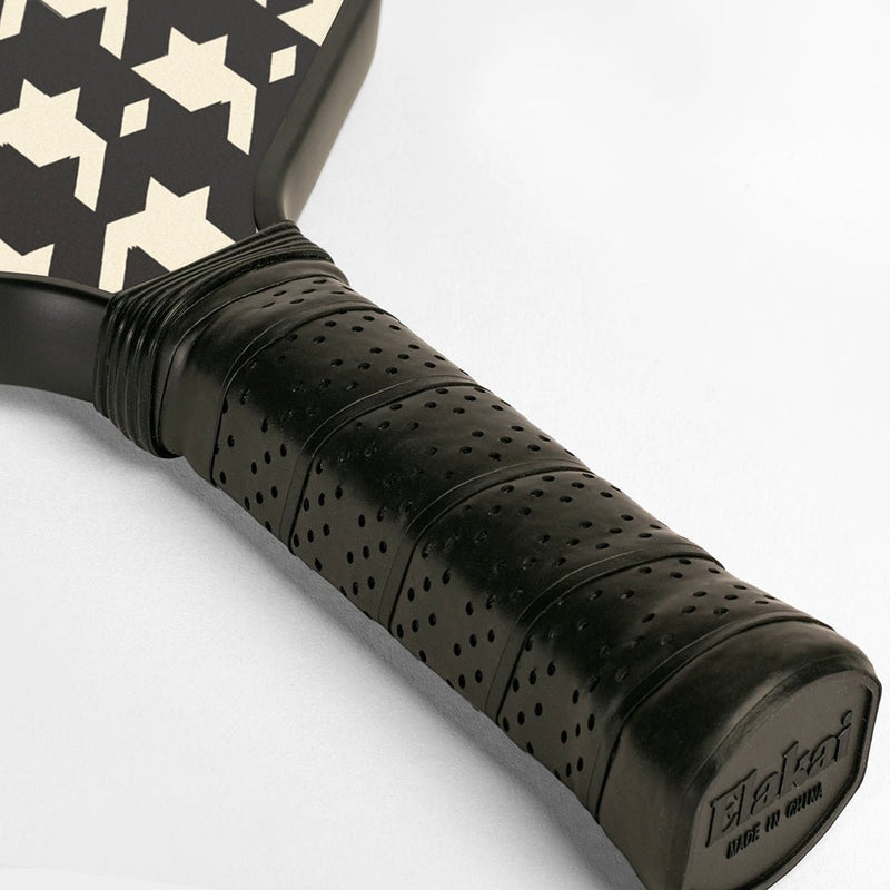 Close-up of a pickleball paddle with black and white patterned face and textured black handle on a light gray background.