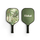 Two pickleball paddles, one with a tropical leaf design and the other with 'Elakai' branding, on a white background.