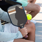 Person holding a pickleball paddle with a wolf design and a yellow ball, sitting on steps.