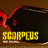 Hand holding a red ping pong paddle with 'SCORPEUS 3S DUAL' branding on a brown background