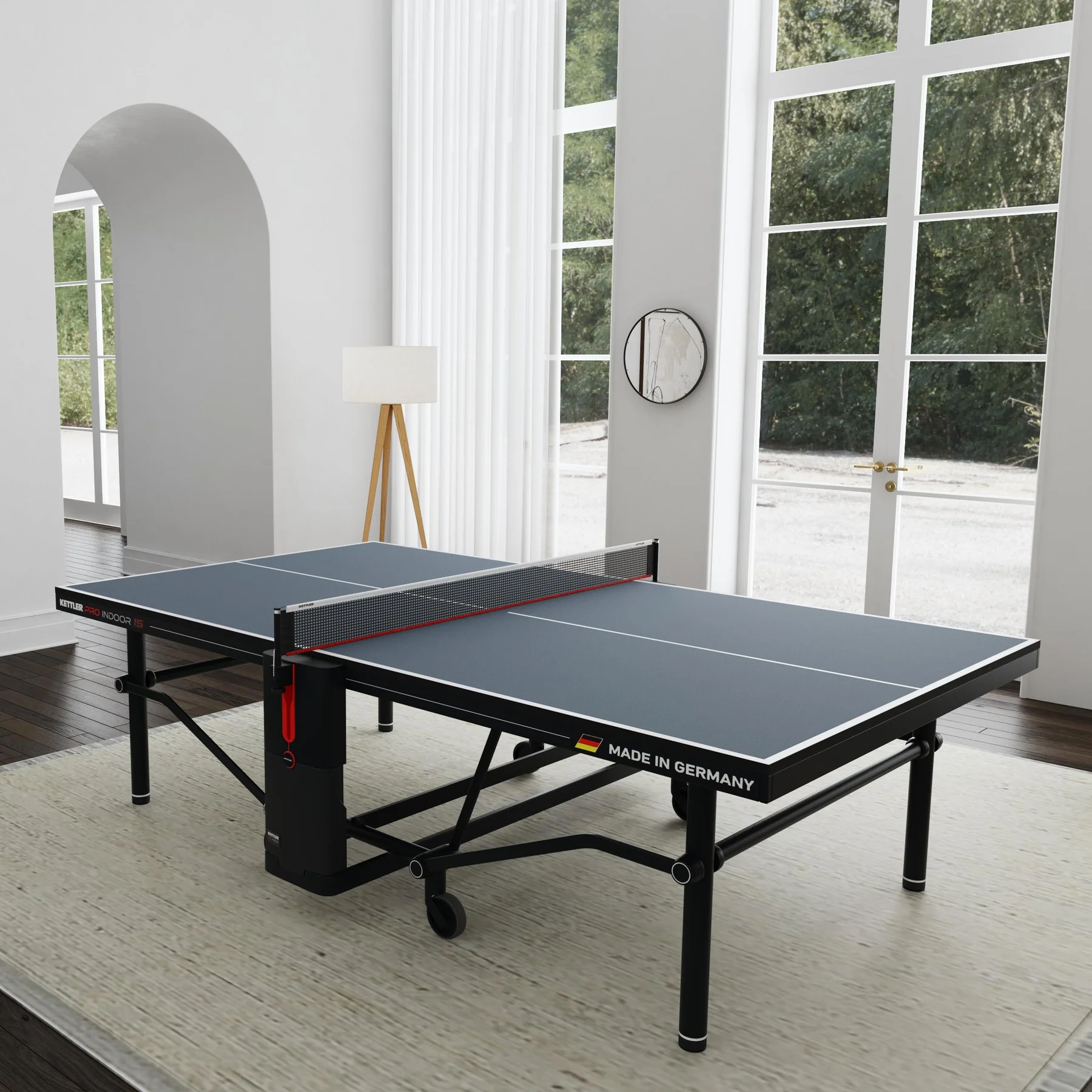 The Kettler Pro Indoor 15 Table Tennis Table sits in a bright room with large windows and light walls.