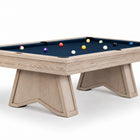 A modern pool table featuring a light natural wood frame and legs, paired with a dark navy blue felt surface and several colorful billiard balls, shown against a plain white background.