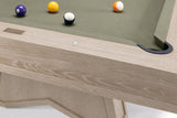Close-up of a wooden pool table showing the light oak frame, green felt surface, and several billiard balls on a white background.