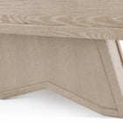 Close-up of a light oak wood table showing the underside of the tabletop and a geometric, angular pedestal base on a white background.