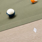 Close-up of a billiards table corner with a green felt surface, wooden side rail, and several pool balls including a yellow ball, a blue-and-white numbered ball, and part of an orange ball.