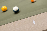 Close-up of a billiards table corner with a green felt surface, wooden side rail, and several pool balls including a yellow ball, a blue-and-white numbered ball, and part of an orange ball.