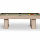 A modern pool table with a light beige wood-grain frame and a sage green felt surface, shown on a clean white background with a few billiard balls on the table.