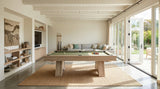 A modern wooden pool table with a green felt surface is centered in a bright, contemporary room with large glass doors, a light wood TV wall, and a woven rug underneath.