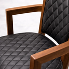Chair with black quilted cushions and wooden armrests on a white background