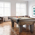 A Brunswick Billiards Glenwood 7' Slate Pool Table in Coffee sits in a bright, art-filled room.