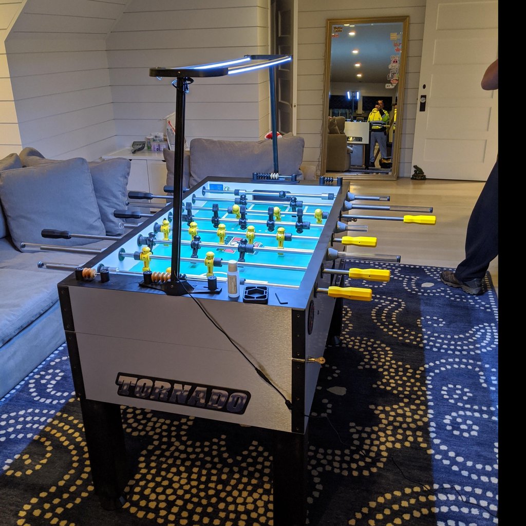 Tornado T-3000 Pro Foosball Table in silver features yellow handles under living room lights.