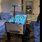 Tornado T-3000 Pro Foosball Table in silver features yellow handles under living room lights.