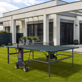 A Kettler Outdoor 6 Tennis Table 4-Player Bundle is on a grassy lawn by a modern house.