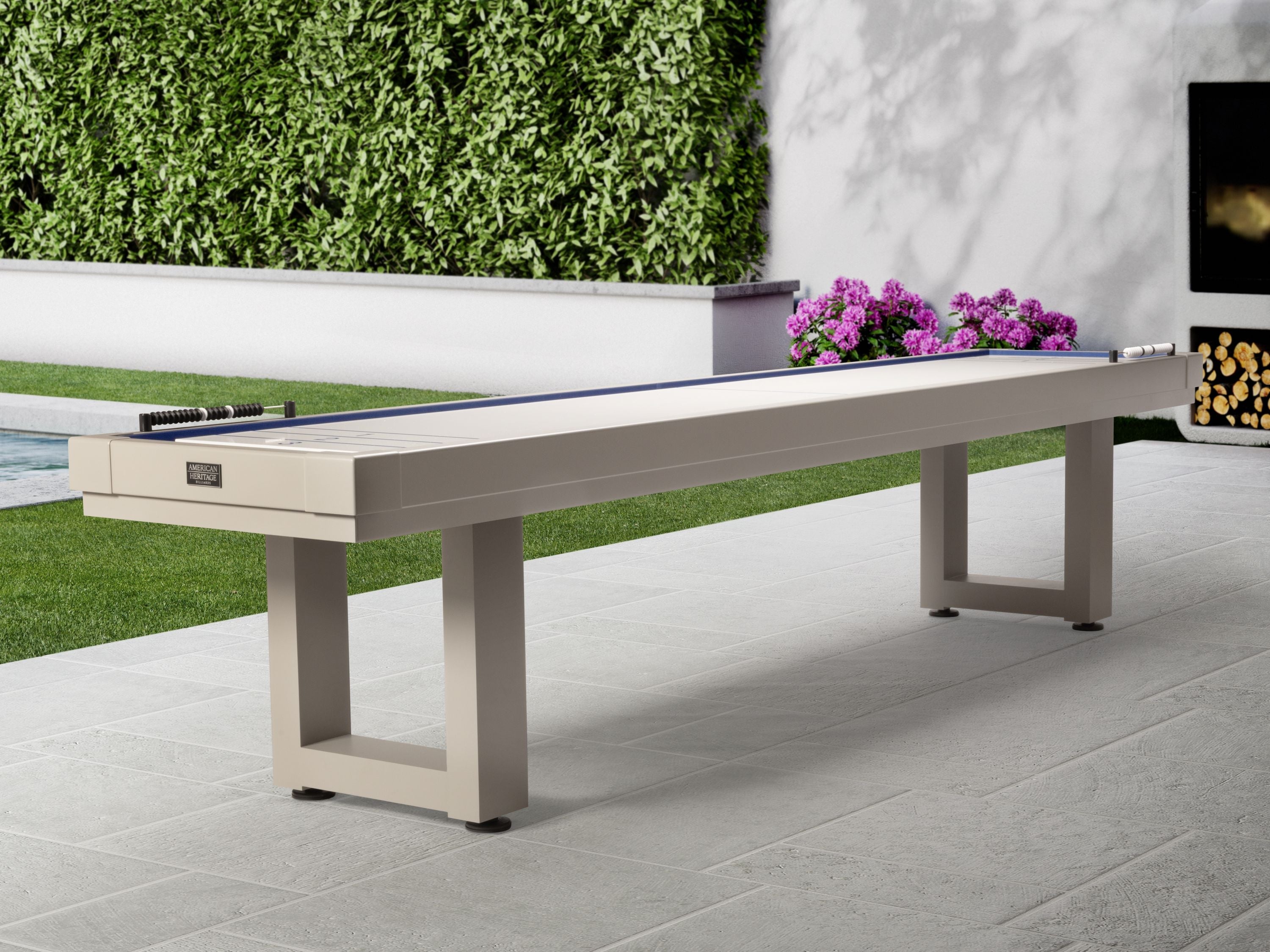 American Heritage Lanai 12' Outdoor Shuffleboard Table in Oyster Grey on patio with greenery.