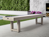 American Heritage Lanai 12' Outdoor Shuffleboard Table in Oyster Grey on patio with greenery.