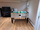 A Tornado Tournament Competition T-3000 Foosball Table in a basement with wood floors and a TV.