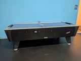 A Dynamo 8' Pro Style Home Air Hockey Table with electronic scorekeeper stands by a blue wall.