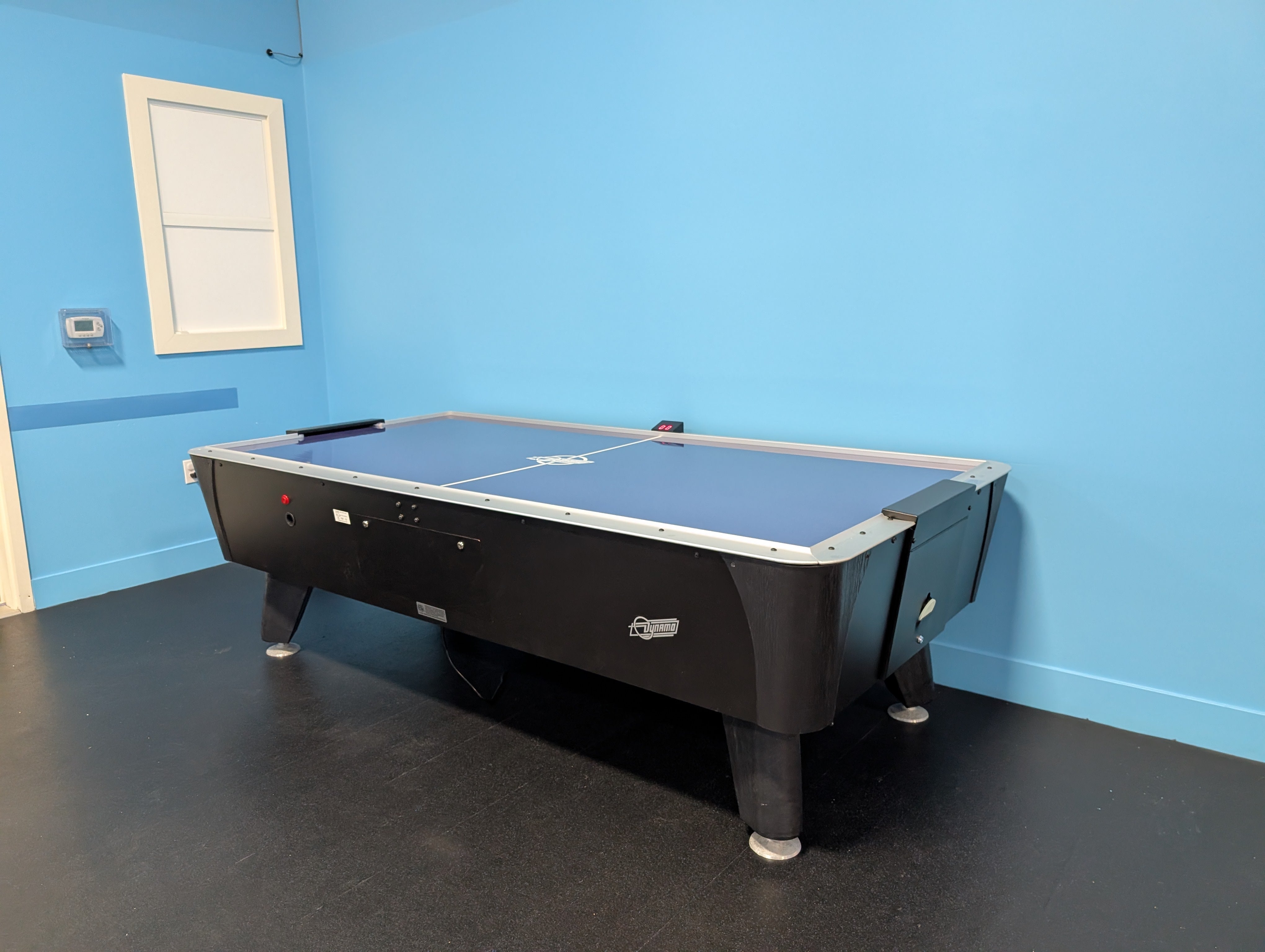 Dynamo 8' Pro Style Home Air Hockey Table by Dynamo in a blue room with black floor and window.