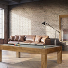 A modern living room with a Brunswick Billiards Parsons 8' Pool Table, leather sofa, and brick walls.
