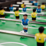 Table football set with players in blue and yellow uniforms on a green playing field.
