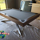 A wooden pool table with a dark gray felt surface, photographed in an indoor room with construction debris and plastic sheeting on the floor. A 'Game World Planet' logo is visible in the lower-left corner.