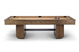 A modern pool table with a medium brown wood grain frame and legs, featuring a tan felt playing surface, a white cue ball, and a rack of colorful billiard balls, shown against a plain white background.