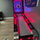 A Bay Tek Skee-Ball Home Arcade Glow with red lights stands on wood floors by a sports flag.