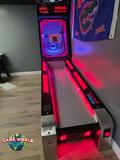 A Bay Tek Skee-Ball Home Arcade Glow with red lights stands on wood floors by a sports flag.