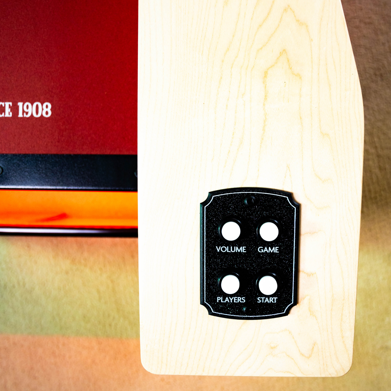 Close-up of a control panel with buttons labeled 'Volume', 'Game', 'Players', and 'Start' on a wooden surface.