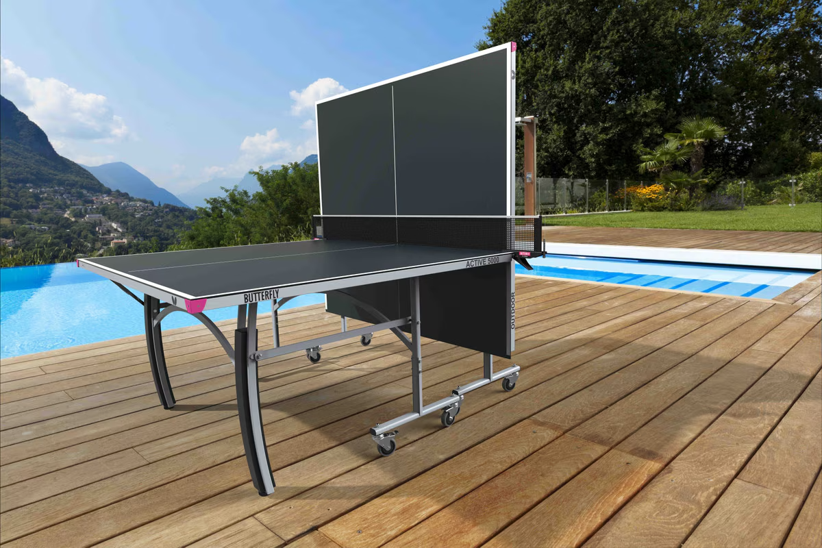 Outdoor ping pong table on a wooden deck with a pool and scenic background