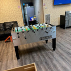 A Tornado T-3000 Professional Foosball Table in silver sits near a black couch and vending machines.