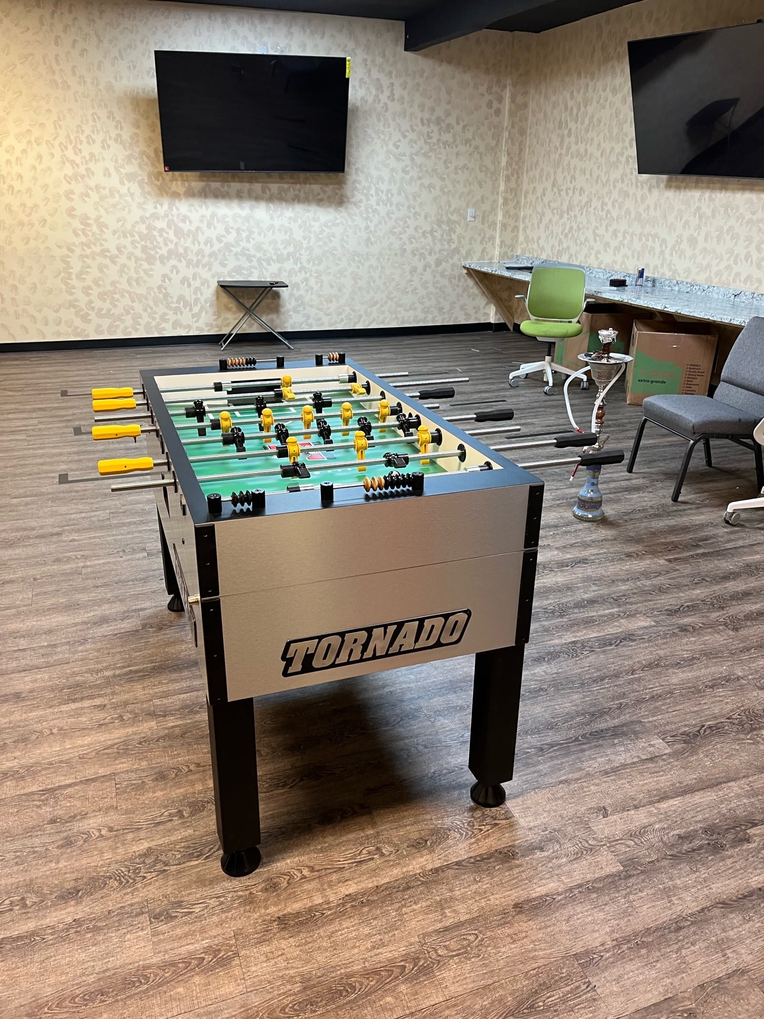 A Tornado T-3000 Pro Foosball Table by Tornado in an office with chairs, TV, and a hookah.