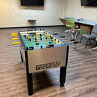 A Tornado T-3000 Pro Foosball Table by Tornado in an office with chairs, TV, and a hookah.