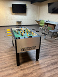 A Tornado T-3000 Pro Foosball Table by Tornado in an office with chairs, TV, and a hookah.
