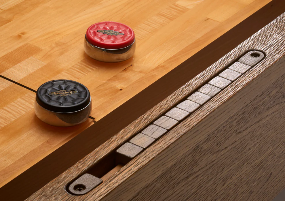 Two pucks on a Brunswick Billiards Botanic 12' Shuffleboard Table in Rustic Dark Brown.