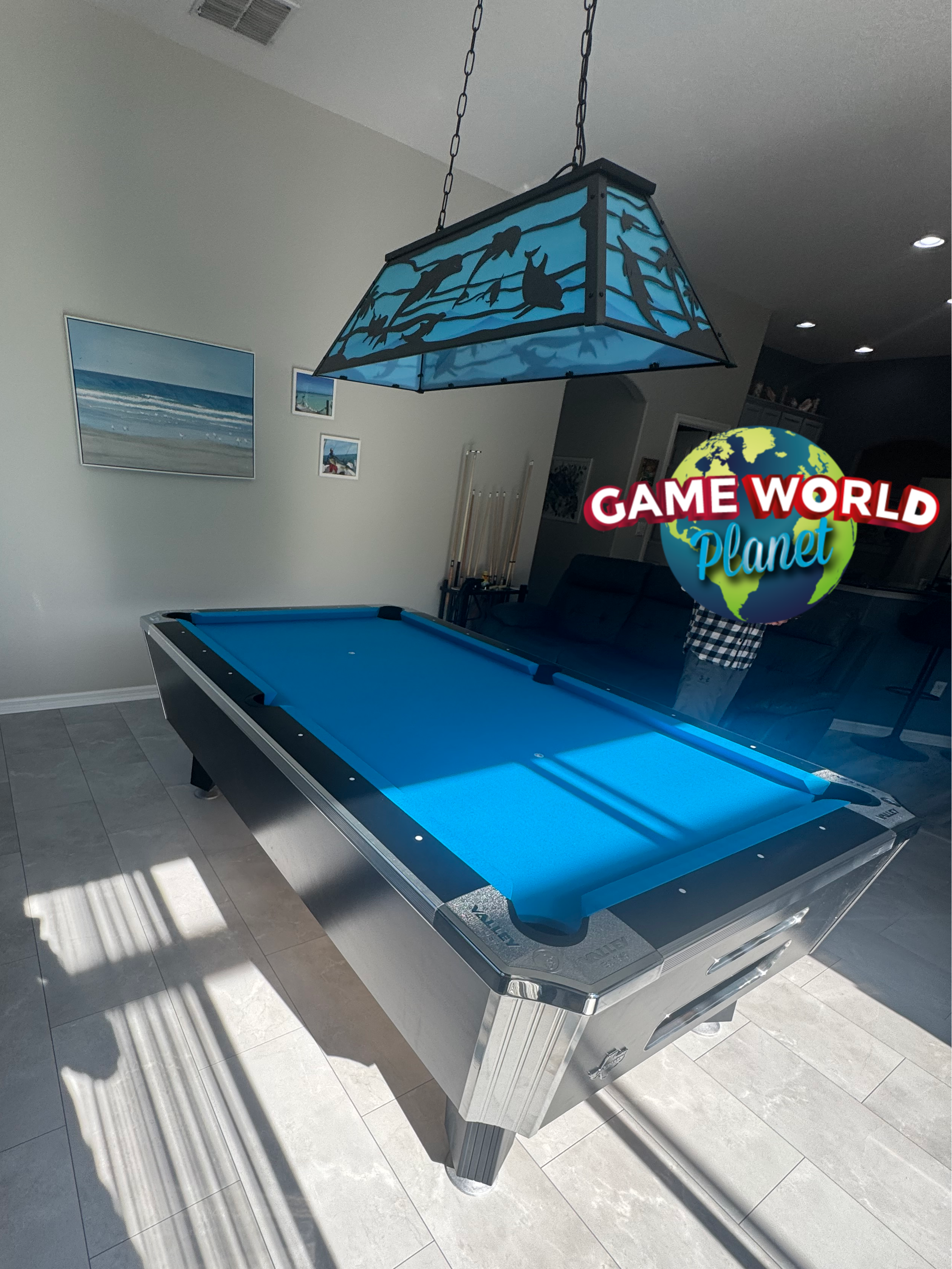 Modern pool table with blue felt in a room with a 'Game World Planet' sign.