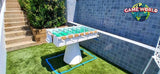 Kettler FAS Ciclope White Outdoor Foosball Table near steps, tiled wall & Game World Planet logo.