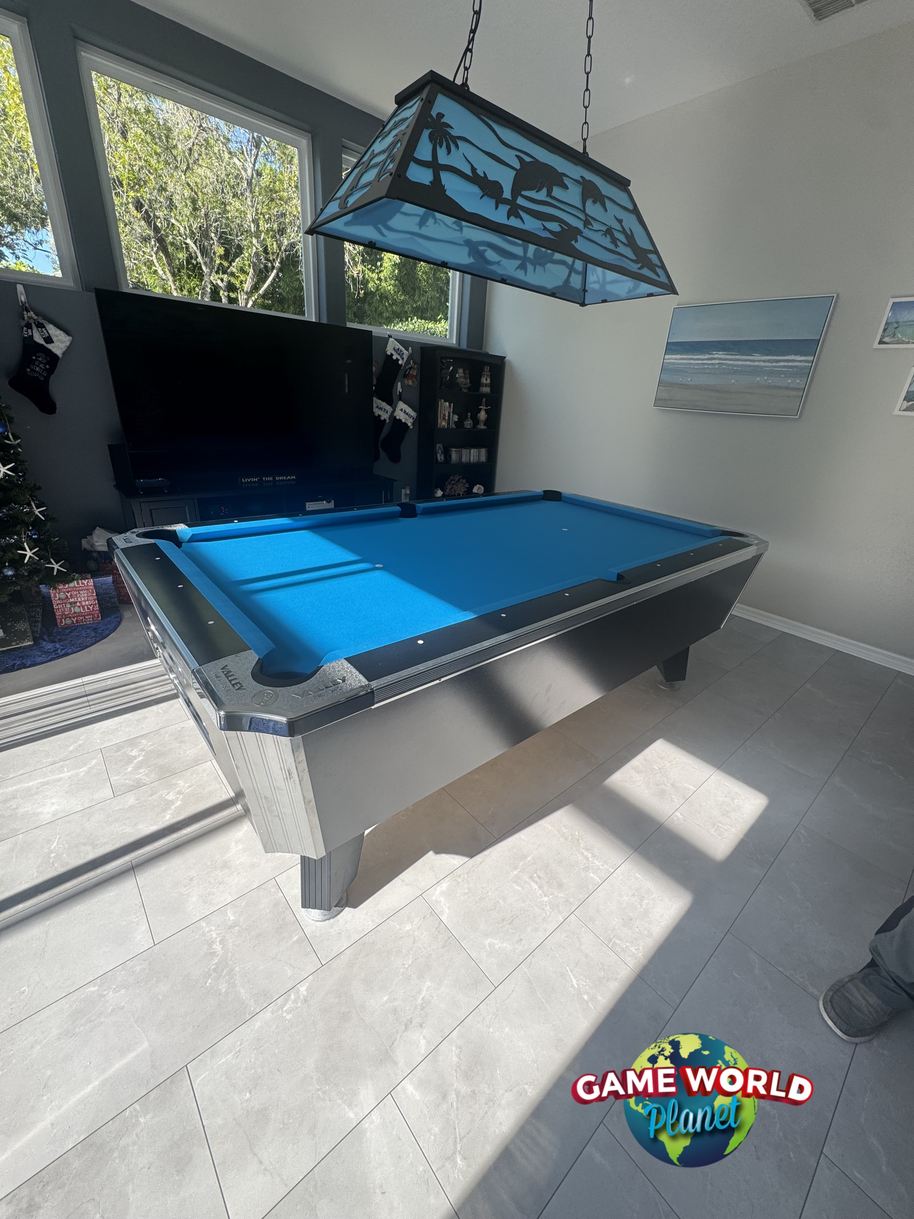 Pool table with blue felt in a room with a television and lamp.