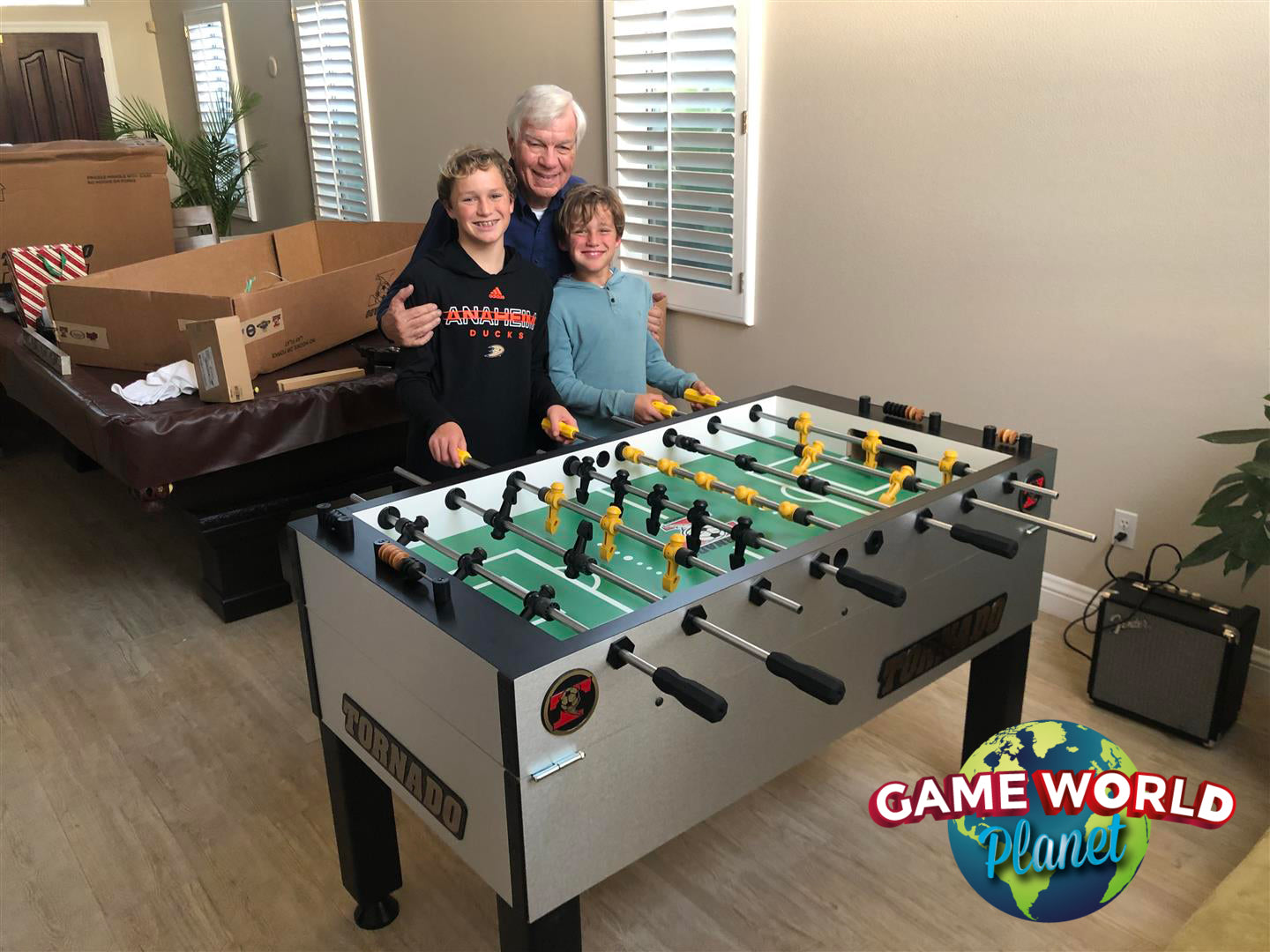 A group stands next to a Tornado Tournament Competition T-3000 Foosball Table in Silver.