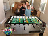 A woman and two children stand by a Tornado T-3000 Silver foosball table amid unpacked boxes.