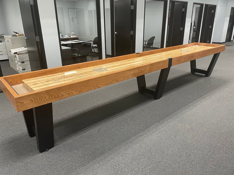 A Champion 12' Fremont Shuffleboard Table stands in an office hallway with desks and doors visible.