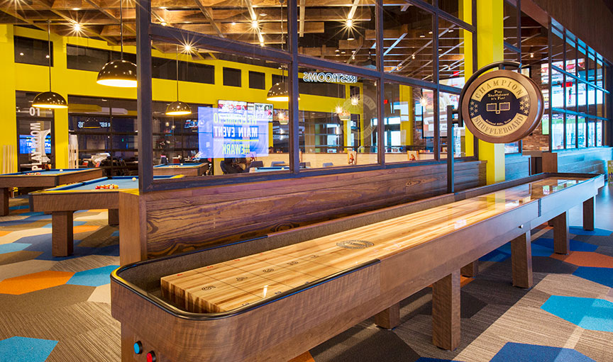 Champion 14' Elite Shuffleboard Table by Champion in a bright game room with yellow walls.