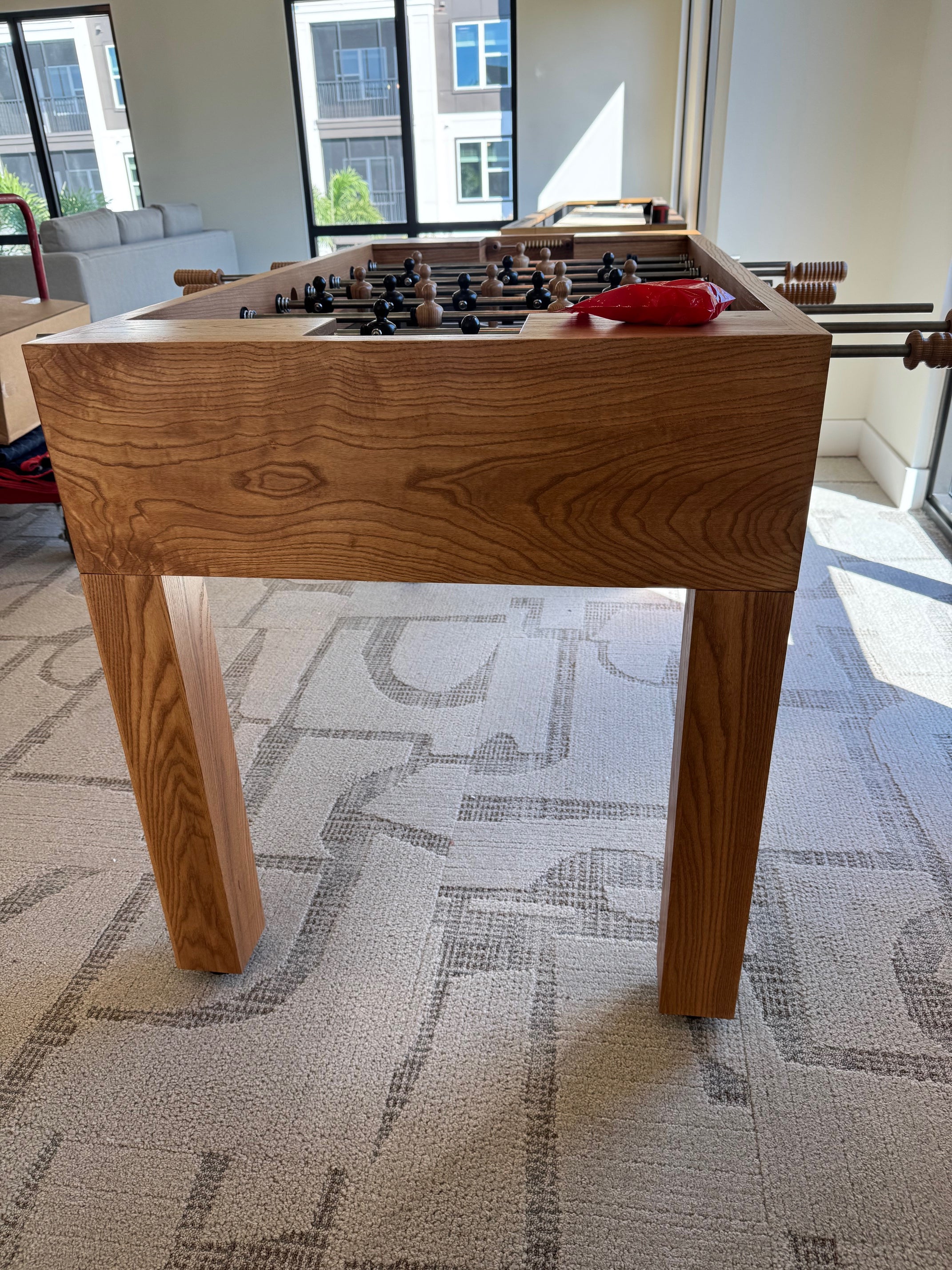 Venture Wooden foosball table in a room with big windows and carpeted floor.