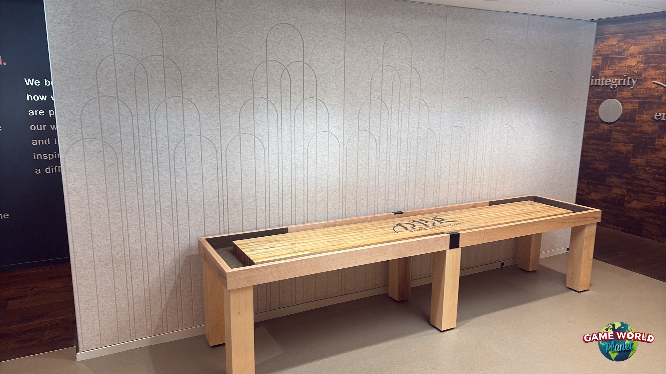 A Champion 12' Richland Shuffleboard Table stands against a light gray patterned wall indoors.