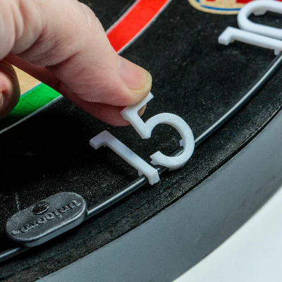 Hand placing a white number '15' on a black surface with a red and green object in the background.