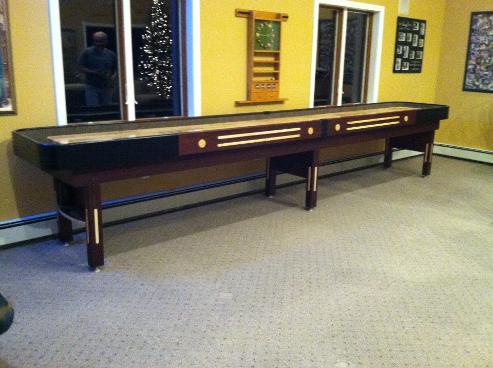 A Champion 9' The Grand Champion Shuffleboard Table sits in a carpeted room with big windows.