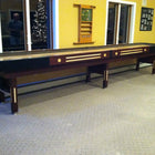 A Champion 9' The Grand Champion Shuffleboard Table sits in a carpeted room with big windows.
