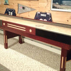 A Champion 9' The Grand Champion Shuffleboard Table in a sports-themed room with framed jerseys.